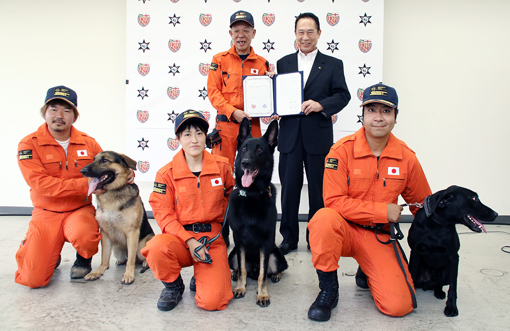 協定書を手にする津田理事長（奥左）と尾花市長（同右）、災害救助犬とハンドラーら