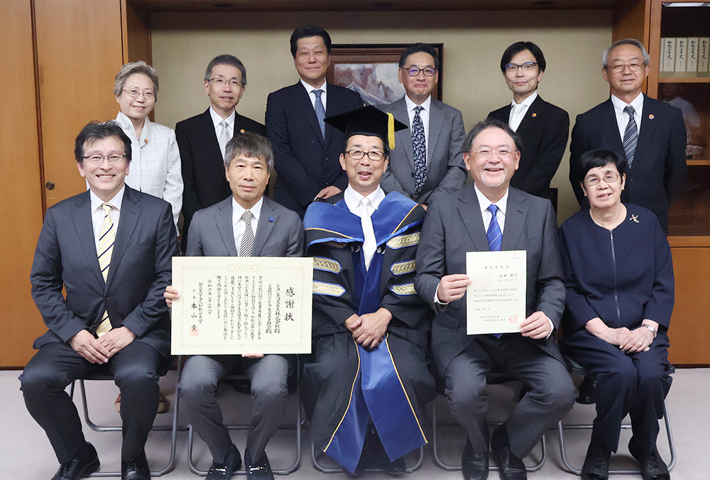 名誉学位記を手に奥田昌孝氏（前列左から４人目）と本山学長（同３人目）ら