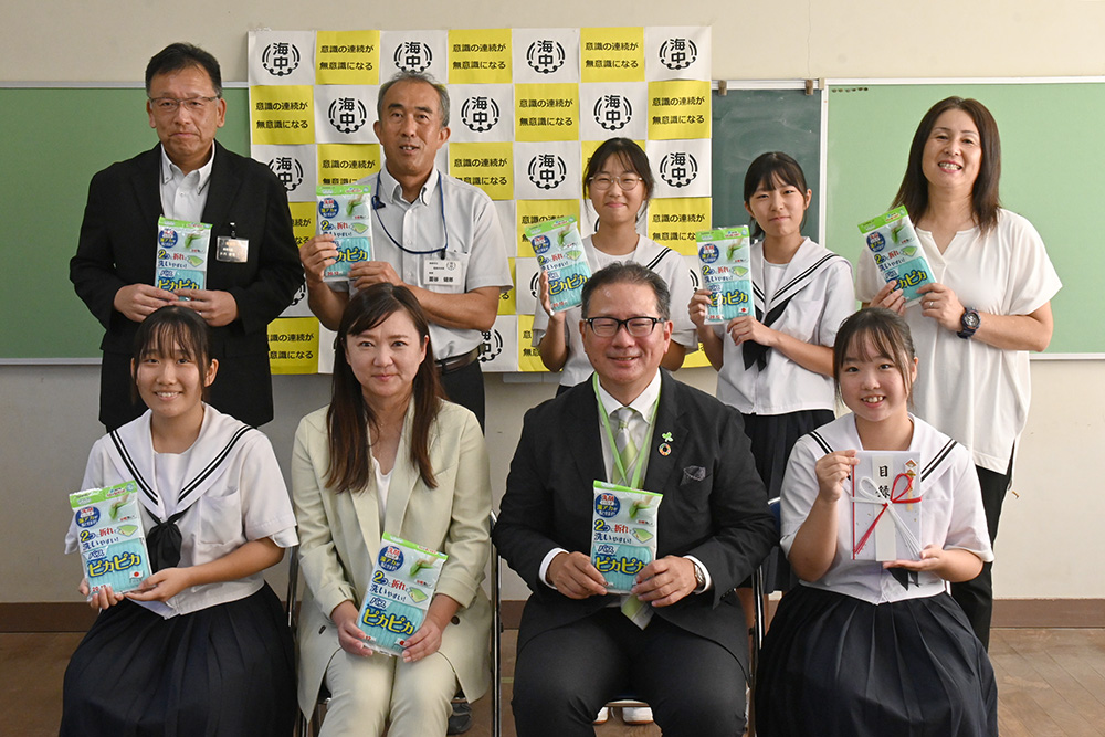 寄贈した日用品を手に角谷社長（前列左から３人目）と生徒ら