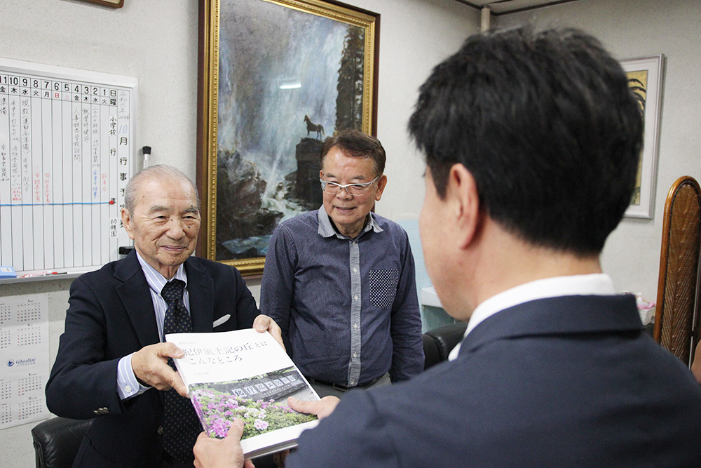 結城校長㊨に写真集を手渡す上岡さん㊧と西本代表