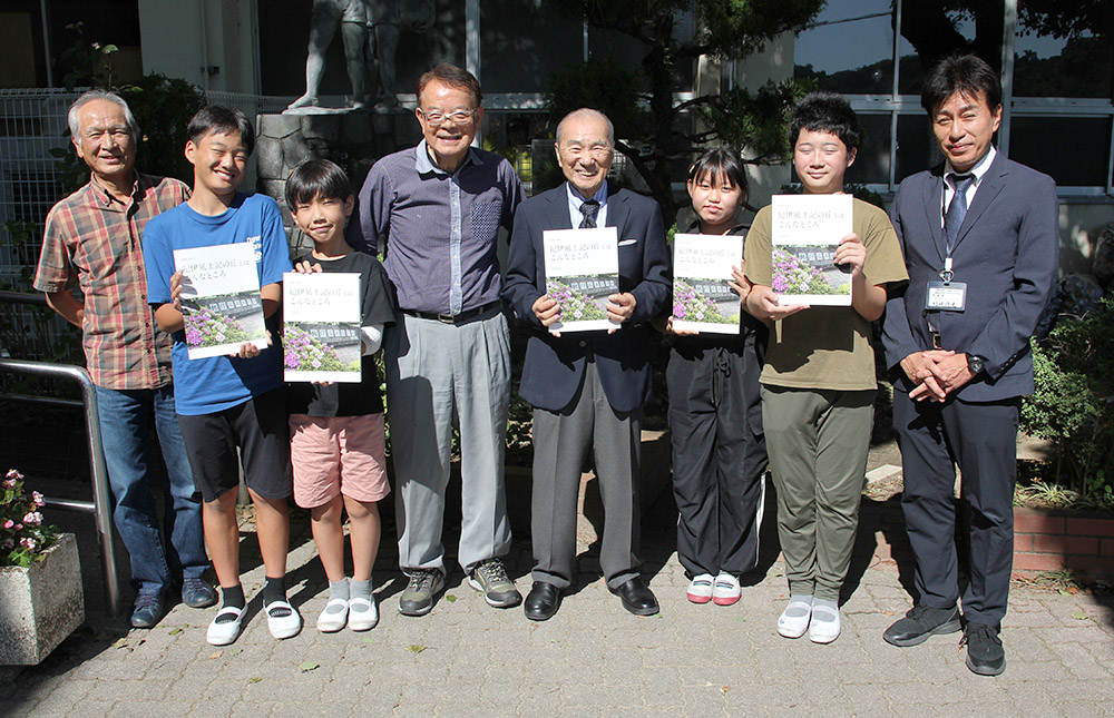 写真集を手に和佐小の児童と上岡さん（左から５人目）、中北さん（同１人目）、西本代表（同４人目）、結城校長㊨