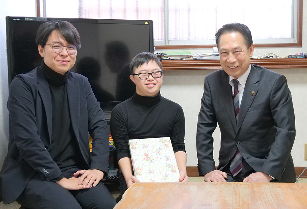 祝いの品を手に笑顔の尾花市長㊨と中野さん、岩橋理事長㊧