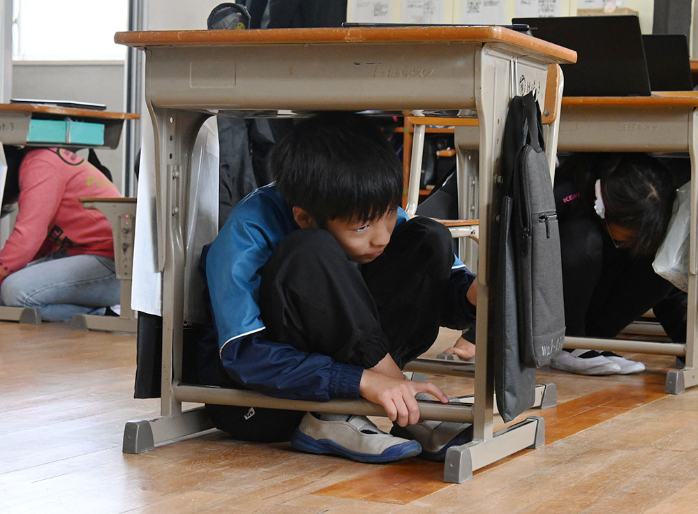 机の下で身をかがめる児童