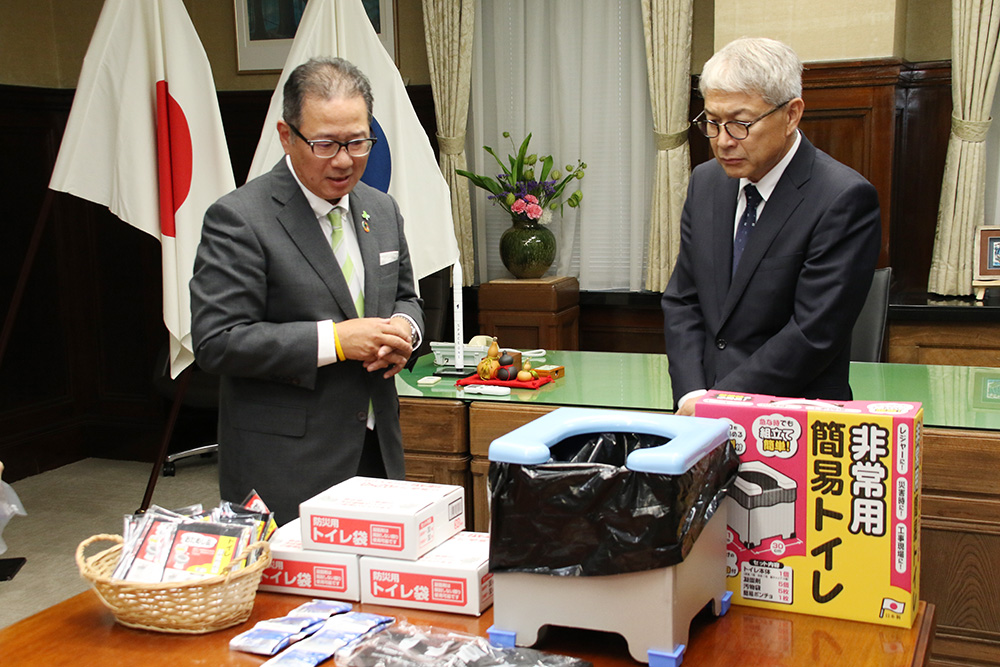 宮﨑知事㊨に携帯トイレの説明をする角谷社長
