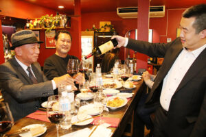 参加者のグラスにワインを注ぐ張社長㊨