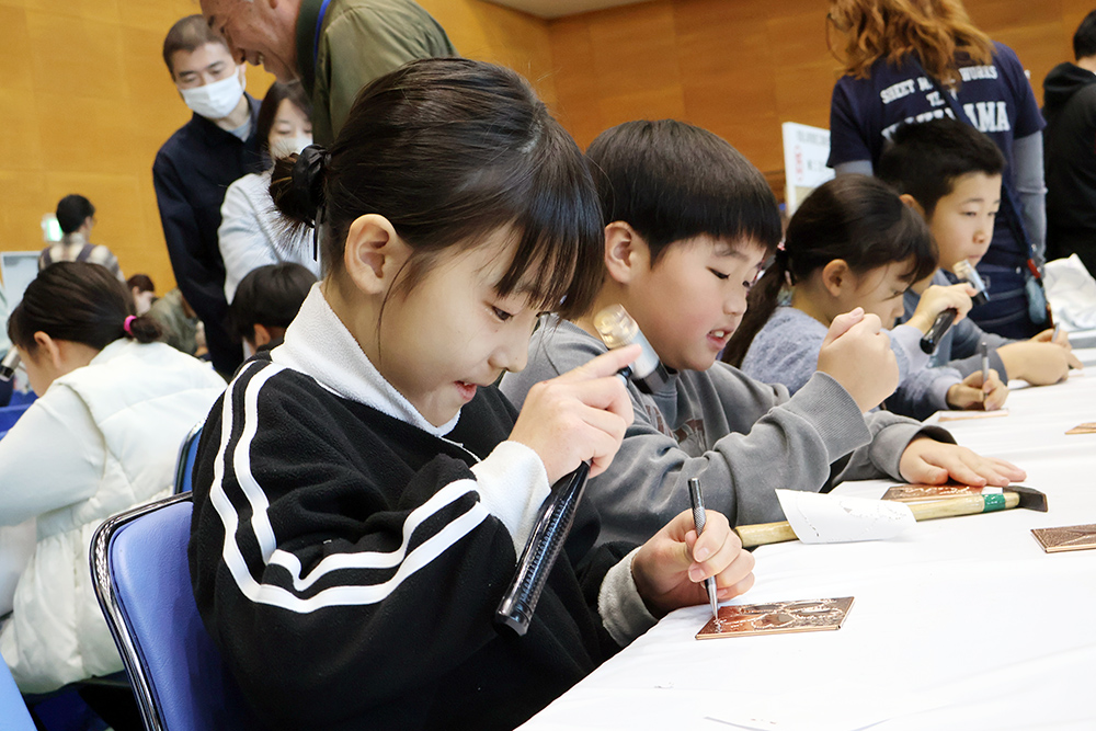 くぎと金づちで銅板に模様を作る子どもたち