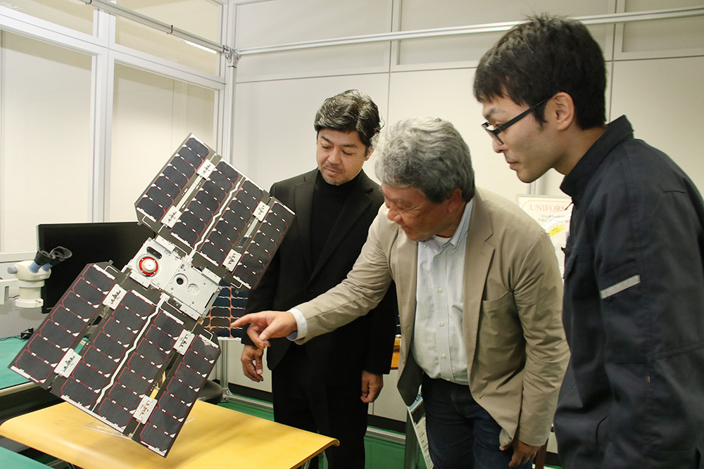 超小型人工衛星のモデルの前で語らう有井社長㊧、秋山教授㊥ら