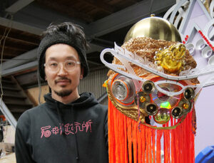 神様の顔の仮面を手に石田さんのアイキャッチ画像