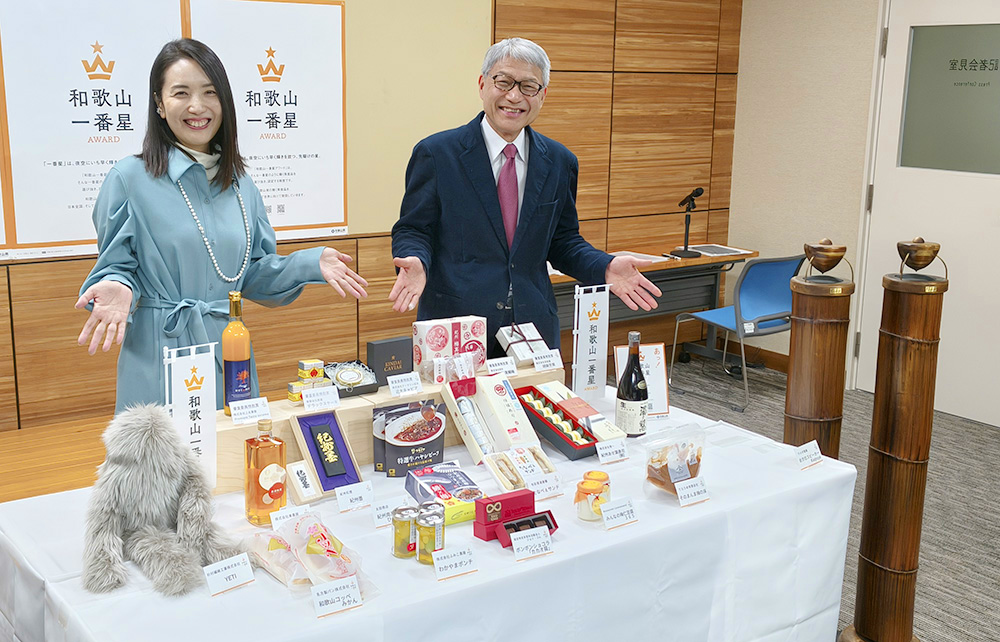 認定商品の前で笑顔の粟飯原委員長㊧と宮﨑知事