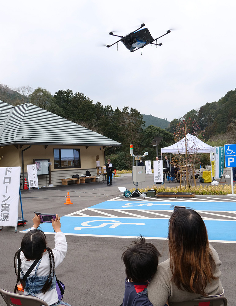 ドローンによる物資輸送訓練を見守る住民ら