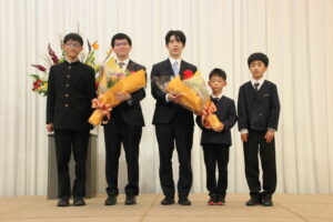 前夜祭で花束プレゼンターの子どもたちと共に藤井王将(中央)、永瀬九段(左隣)
