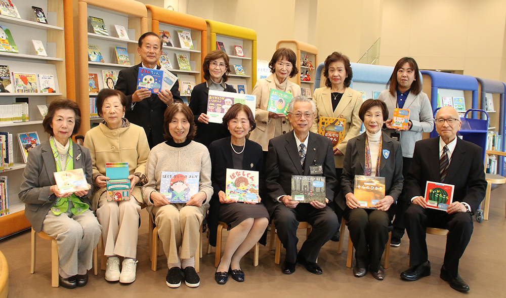 寄贈した絵本を手に笑顔の川端会長（前列中央）、神出市長（右隣）ら