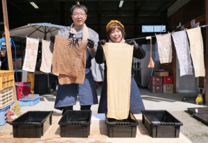 自慢の柿渋染めタオルを手に笑顔の山下さん夫妻