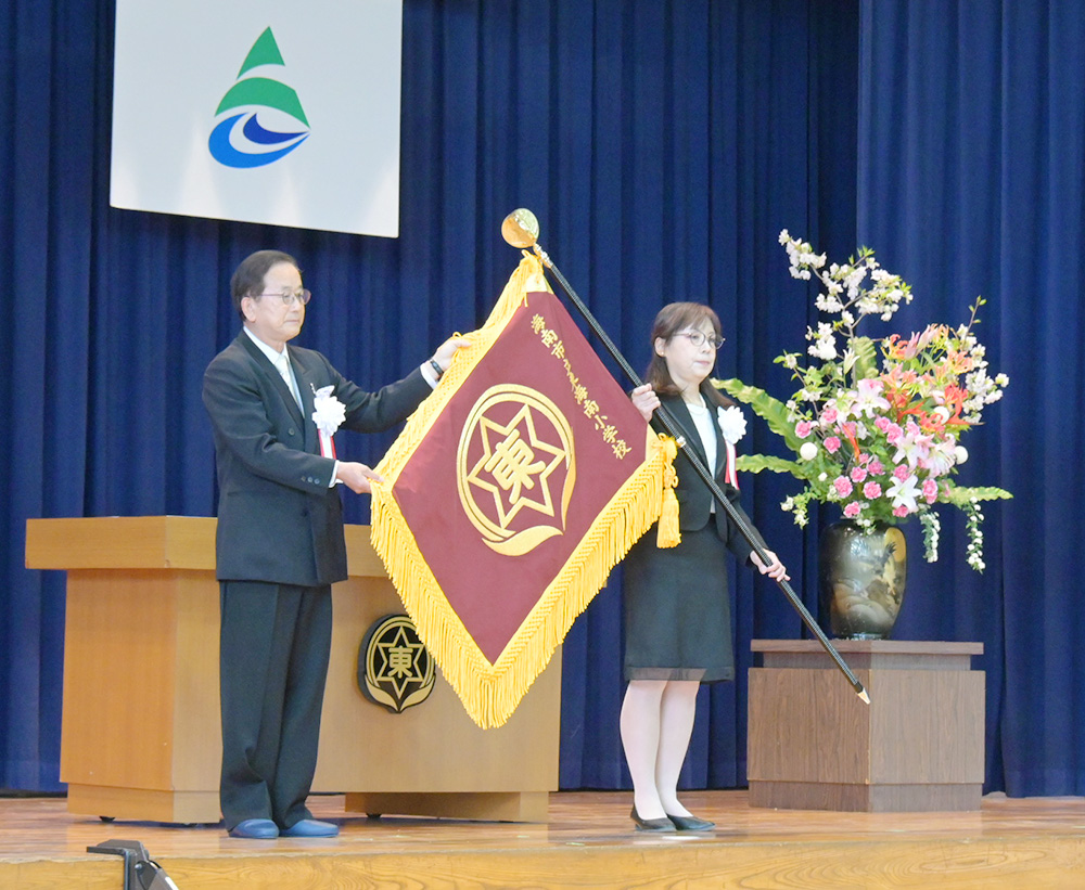 校旗を持つ沼田校長㊨と西原教育長