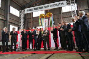 記念のくす玉を割り、拍手に包まれる小嶋社長(中央)と出席者ら