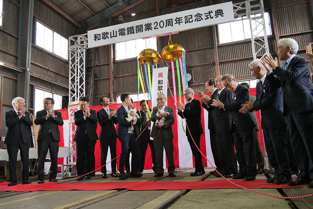 記念のくす玉を割り、拍手に包まれる小嶋社長(中央)と出席者ら