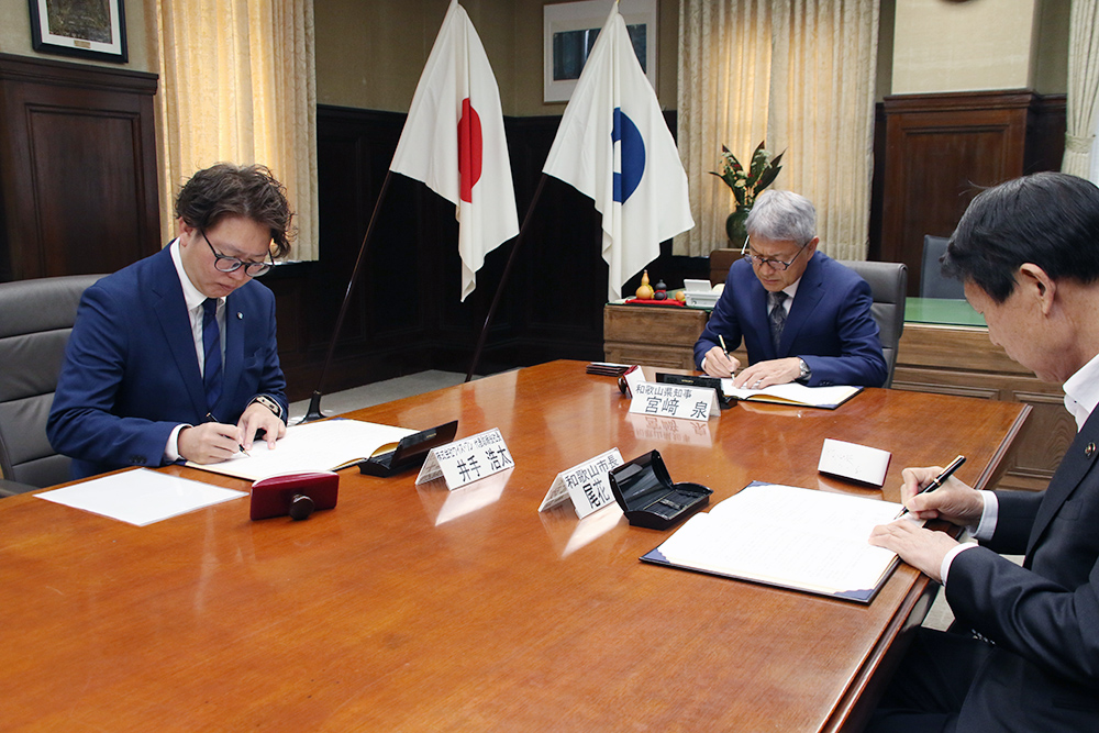 協定書に署名する井手社長㊧、尾花市長㊨、宮﨑知事