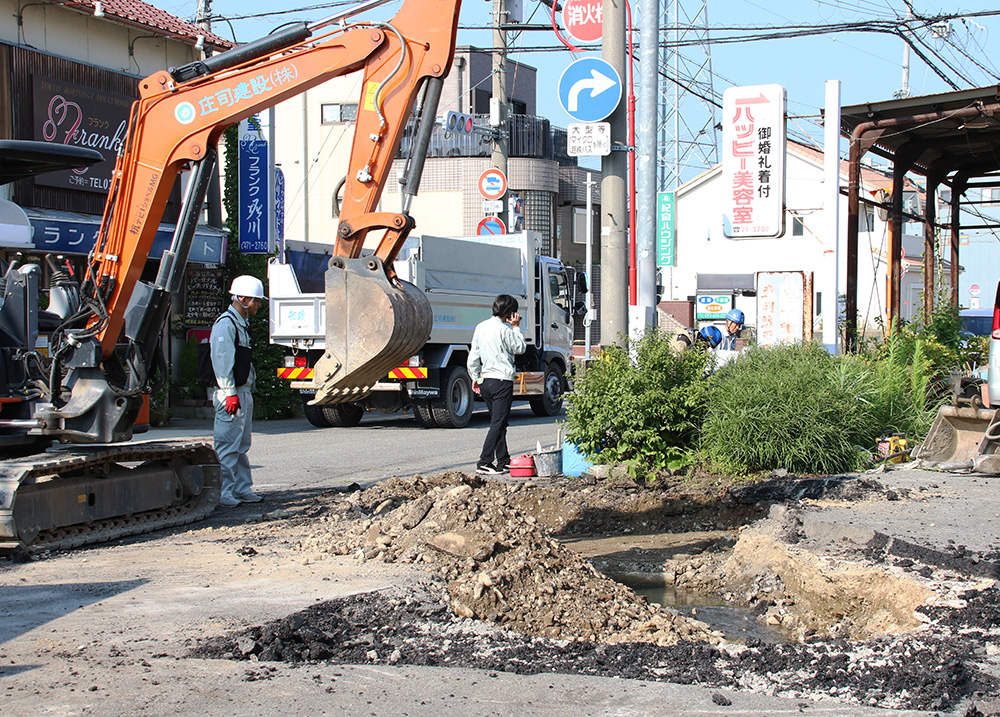 原因の調査が行われている陥没現場。掘削した路面下に用水路がある(21日午後4時15分)