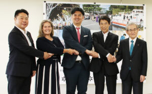 笑顔で手をつなぐ出席者（左から）梶谷社長、デンジャーフィールド校長、根岸理事長、尾花市長、田中会長