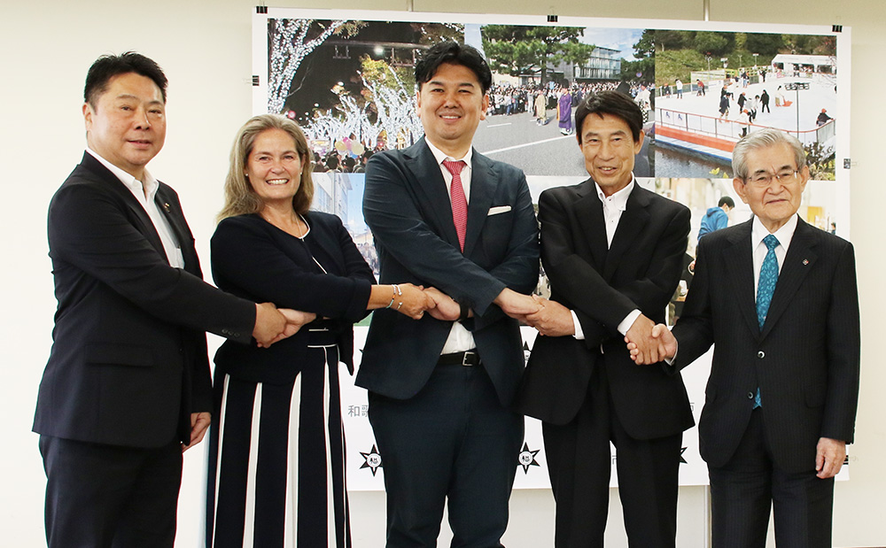 笑顔で手をつなぐ出席者(左から)梶谷社長、デンジャーフィールド校長、根岸理事長、尾花市長、田中会長