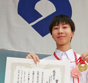 表彰状とメダルを手に、最優秀賞に選ばれた原さんのアイキャッチ画像