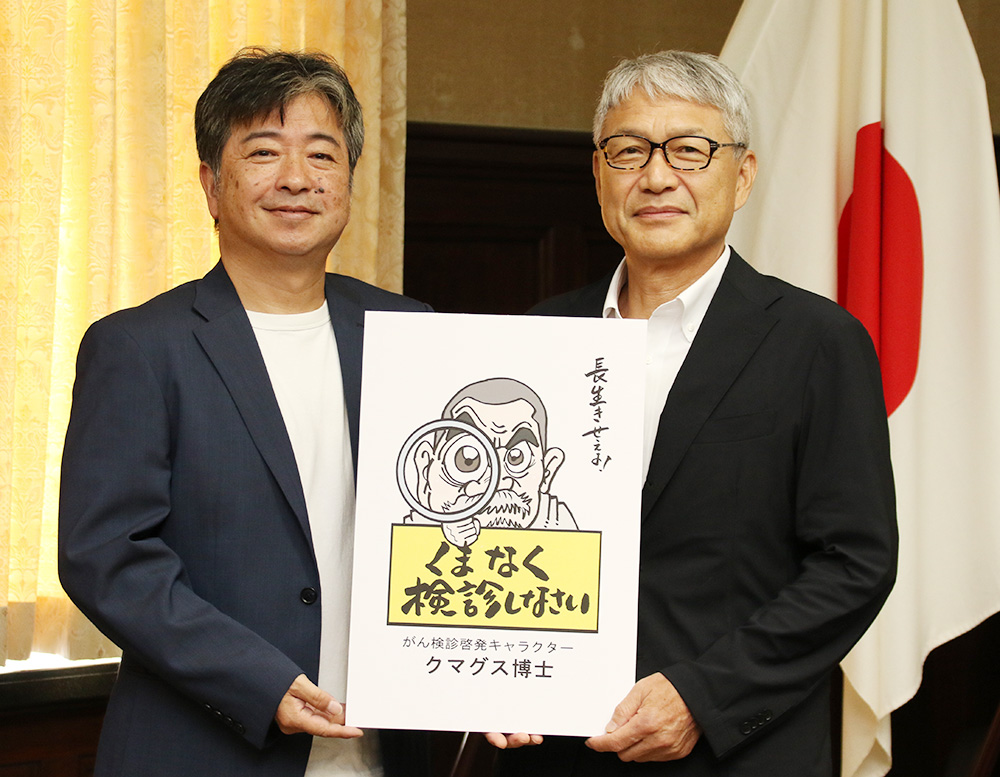 がん検診啓発キャラクター「クマグス博士」のパネルを手にマエオカさん㊧と宮﨑知事