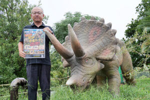 恐竜の横でパークをPRする平松駅長